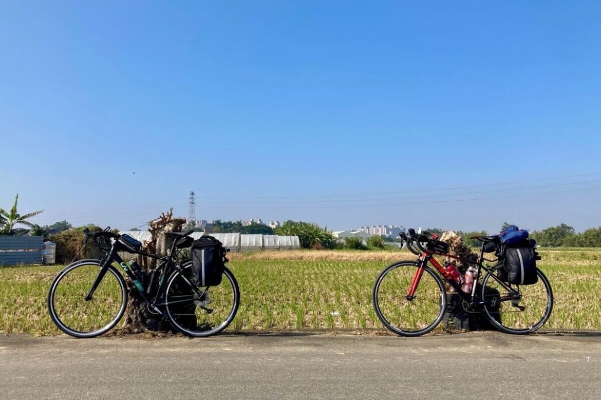 藍天無雲，兩台單車停靠在田地旁的道路邊