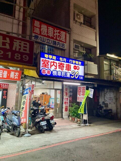 晚上時招牌發亮的寄車店，店門口停放兩輛機車