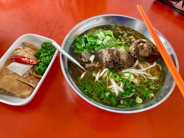 一碗牛肉麵和一盤雞肉放在紅色桌面上