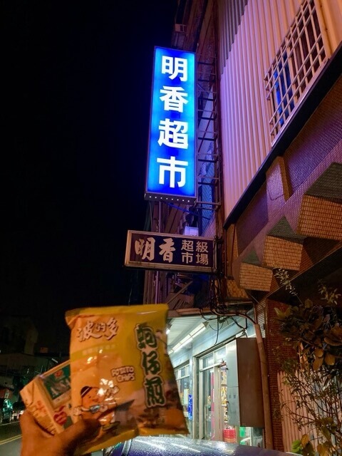 在超市的藍色招牌前面單手拿餅乾和飲料