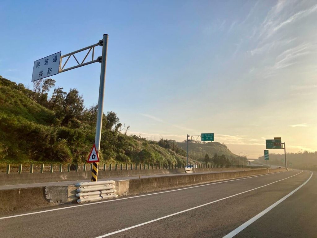 夕陽、公路和標示爬坡道終點的路牌