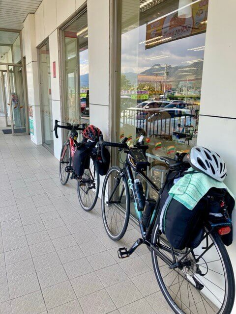 兩台單車靠在超商外的牆面上，毛巾固定在單車的馬鞍袋上